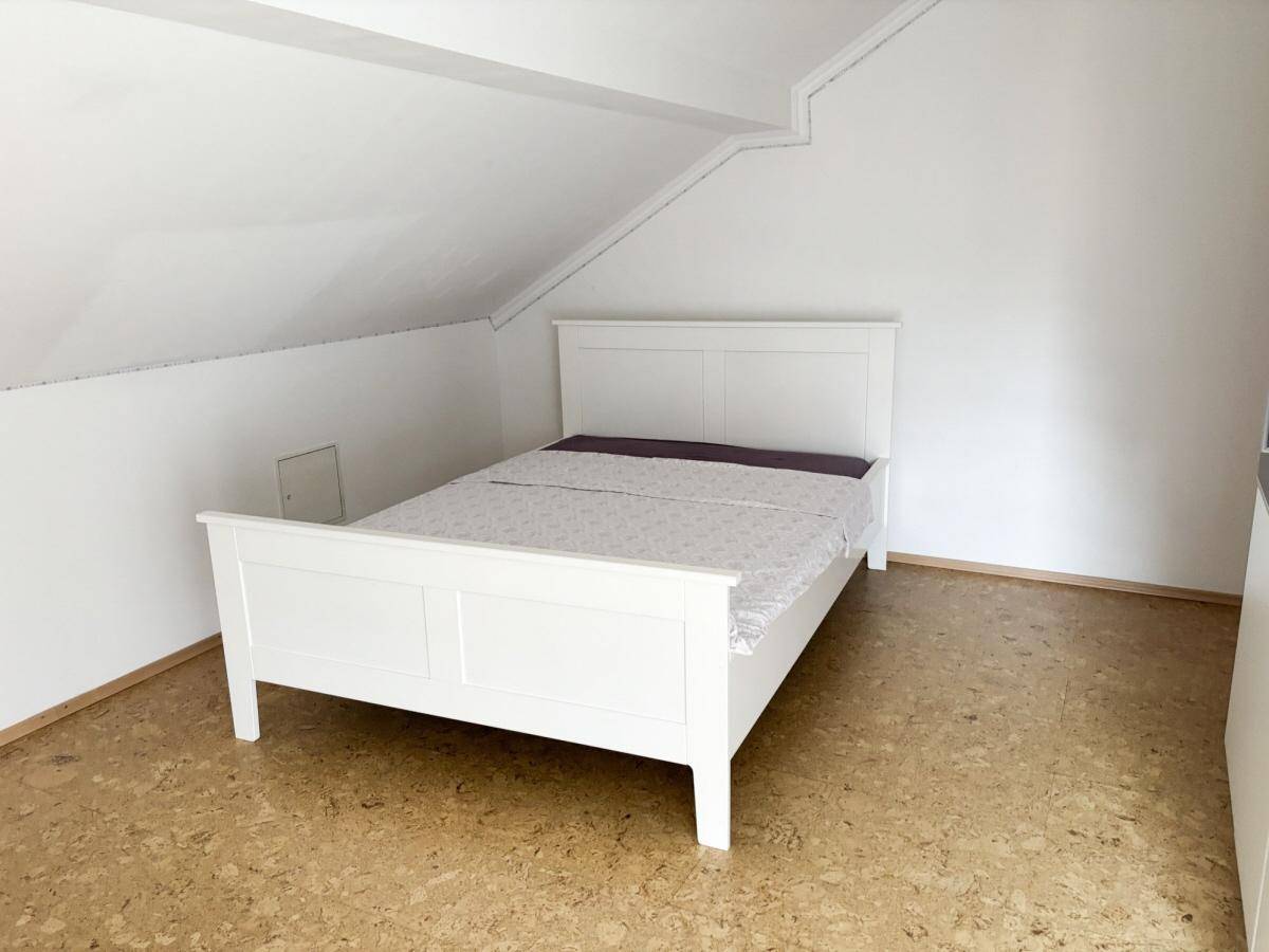 Helles Schlafzimmer im Dachgeschoss mit weißem Bettgestell und Korkboden.