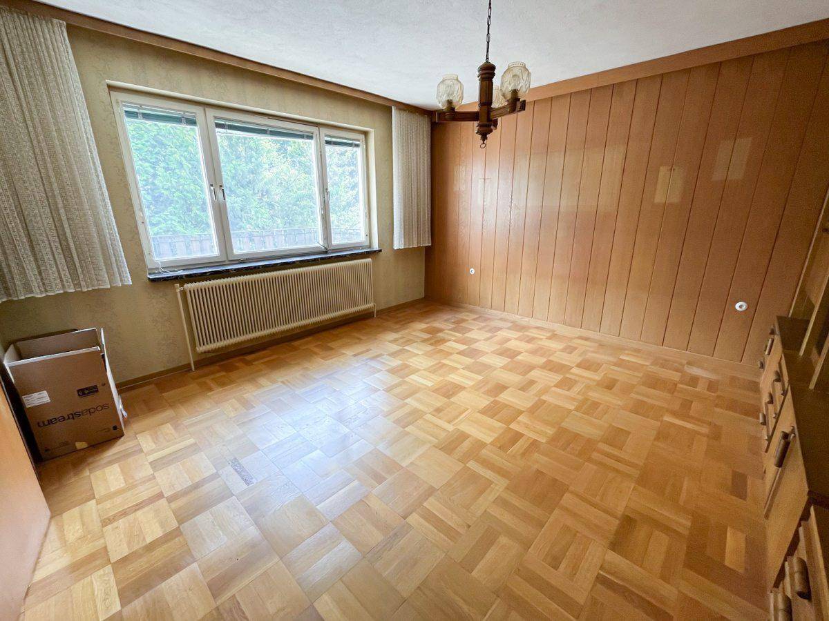 Heller Raum mit Fischgrätparkett, Holzvertäfelung und großem Fenster.
