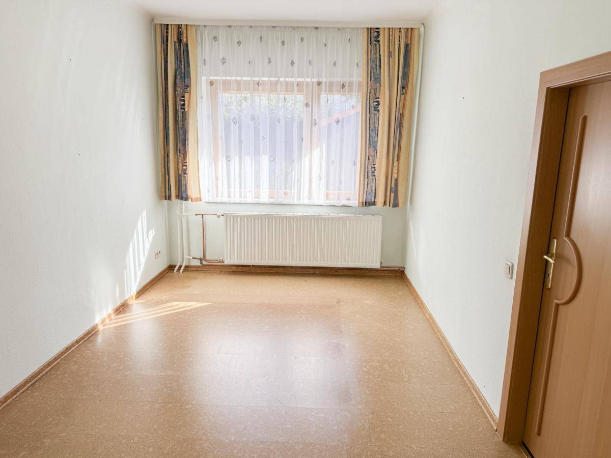 Helles Schlafzimmer mit großem Fenster, Laminatboden und neutralen Wänden, bereit zur individuellen Gestaltung.