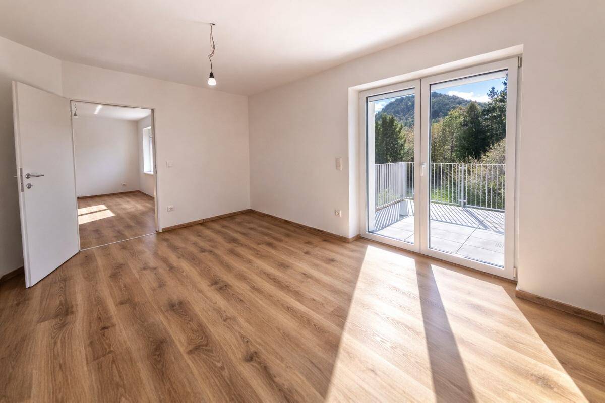 Lichtdurchfluteter Raum mit Laminatboden und direktem Zugang zu einem Balkon mit Bergblick.