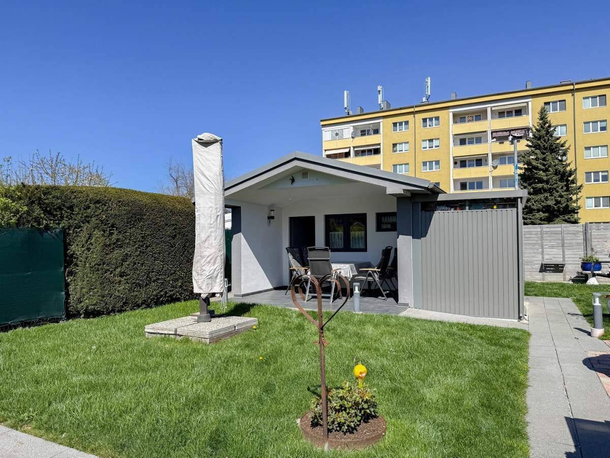 Gepflegter Garten mit Rasenfläche und einer überdachten Terrasse, geschützt durch einen großen Sonnenschirm.