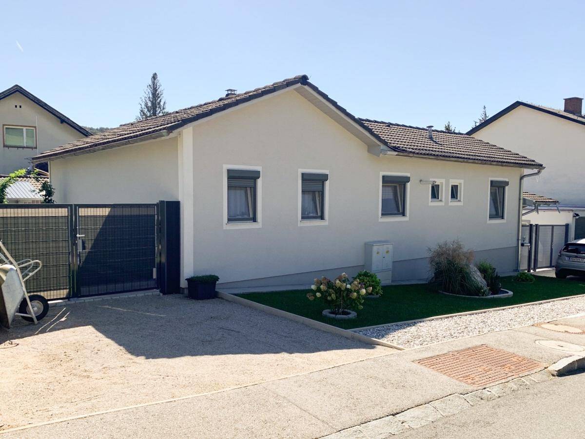 Ansicht des modernen Einfamilienhauses von der Straße mit Vorgarten, Zufahrt und Rollläden an den Fenstern.