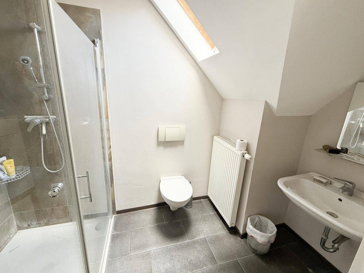 Modernes Badezimmer im Dachgeschoss mit Dusche, WC, Waschbecken und Dachfenster.