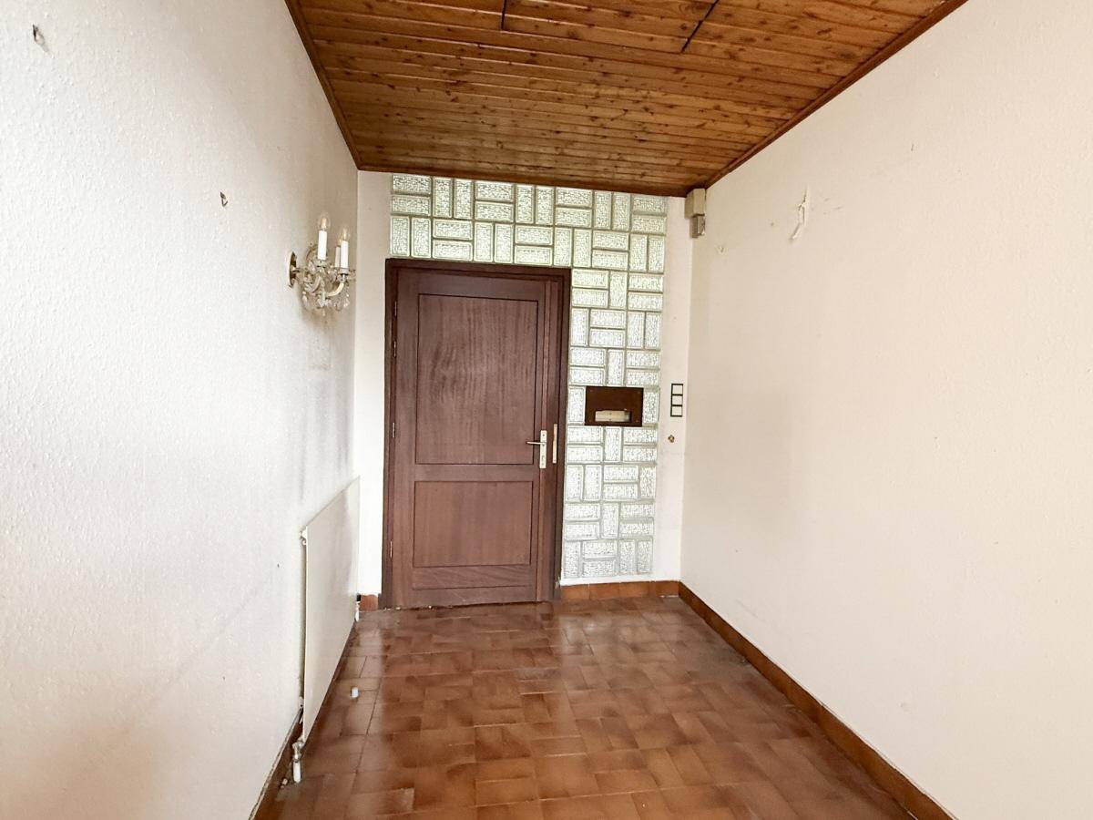 Eingangsbereich mit Holzdecke, Terrakotta-Fliesen und Glasbausteinwand, die Licht spendet.
