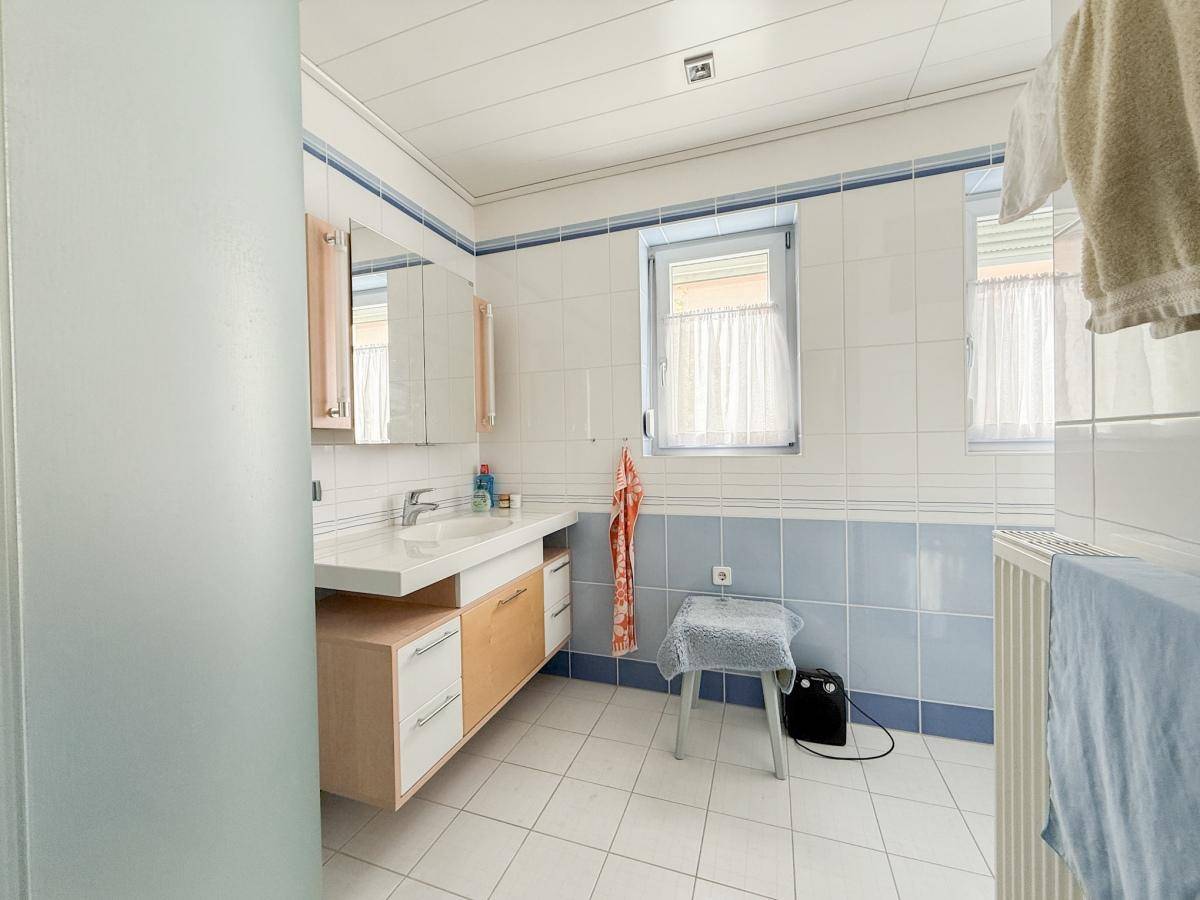 Badezimmer mit blau-weißen Fliesen, Einzelwaschbecken und zwei Fenstern für Tageslicht.