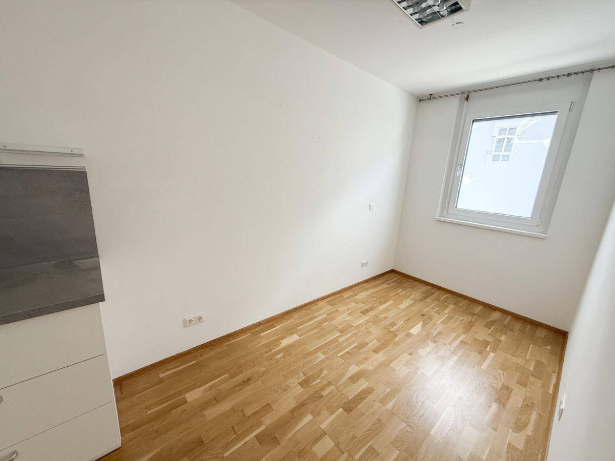 Leeres Zimmer mit hellem Holzparkett und einem Fenster, bereit zur individuellen Gestaltung.