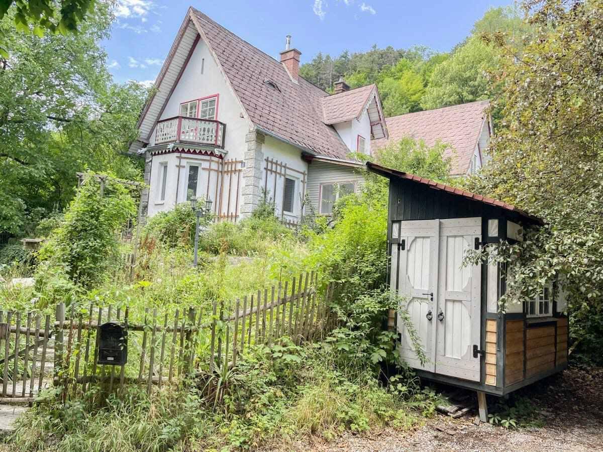 Historisches Haus mit Balkon und einem kleinen, rustikalen Schuppen im verwilderten Garten.