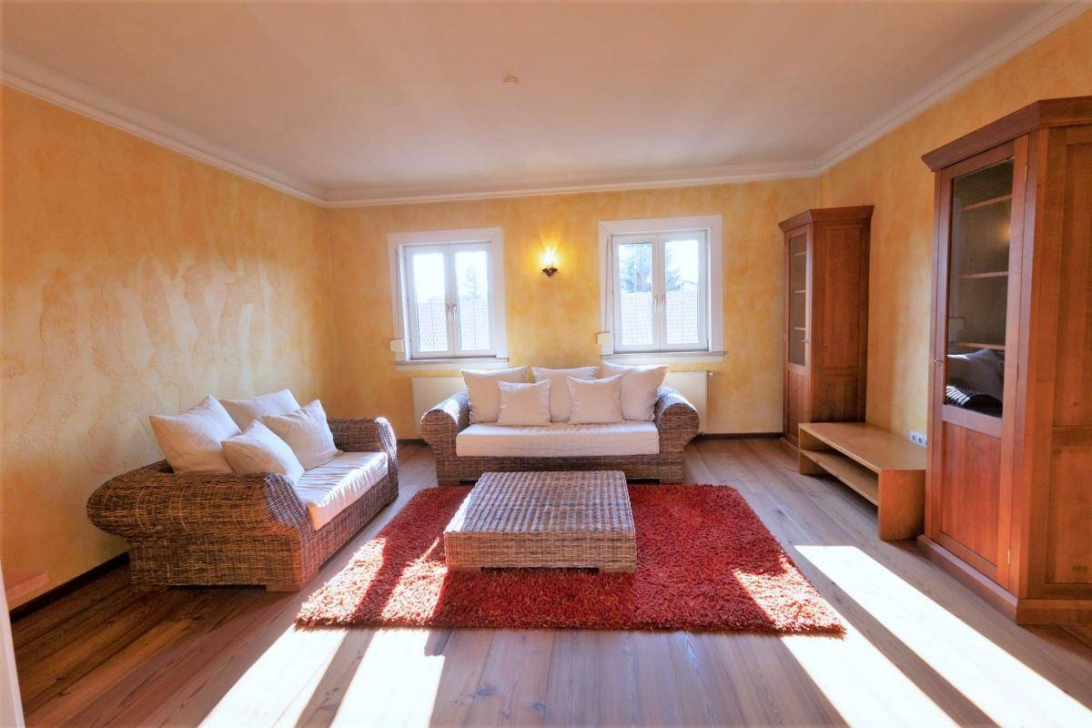 Geräumiges Wohnzimmer mit Korbmöbeln, Holzboden und einem Vitrinenschrank.