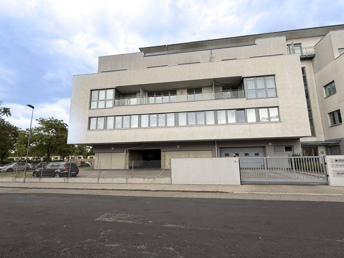 Modernes Geschäftsgebäude mit mehreren Etagen, Balkonen und Parkplätzen davor.