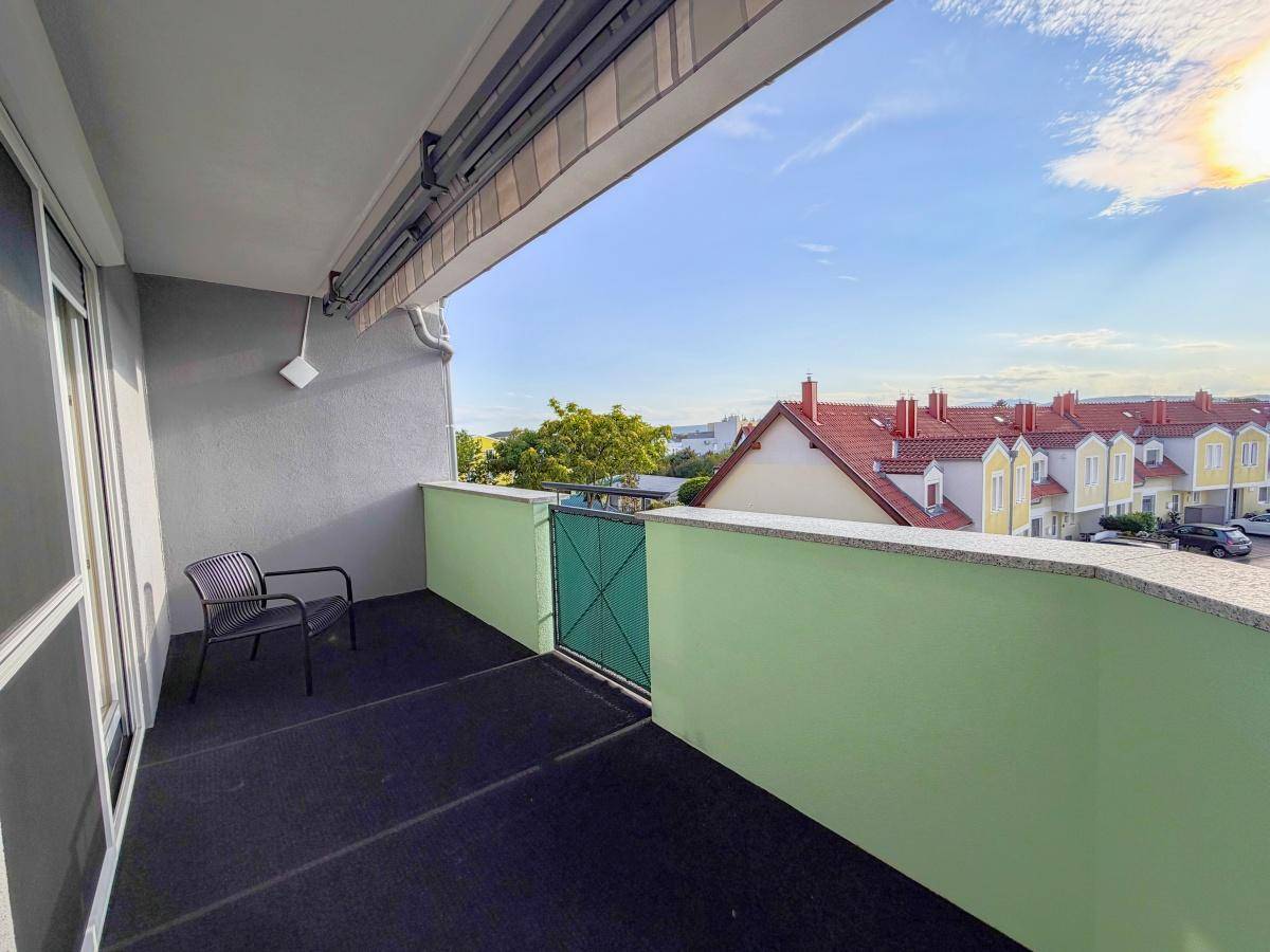 Sonniger Balkon mit Blick auf die umliegenden Häuser und den Himmel.