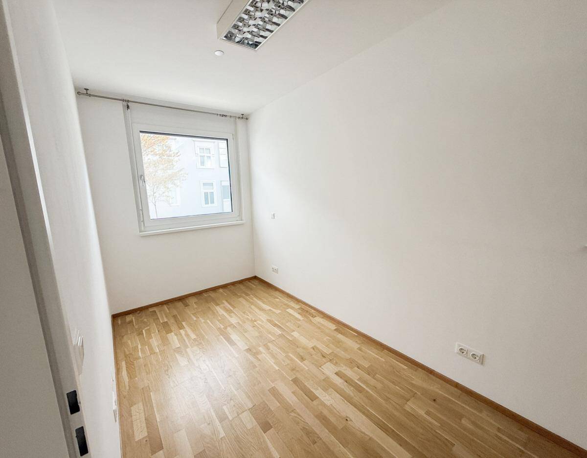 Freundliches Zimmer mit hellem Holzparkett und einem Fenster, vielseitig nutzbar.