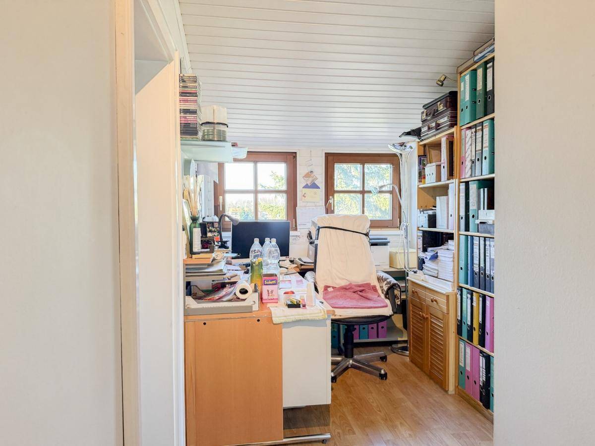 Heller Büroraum mit Holzpaneeldecke, zwei Fenstern und viel Stauraum.