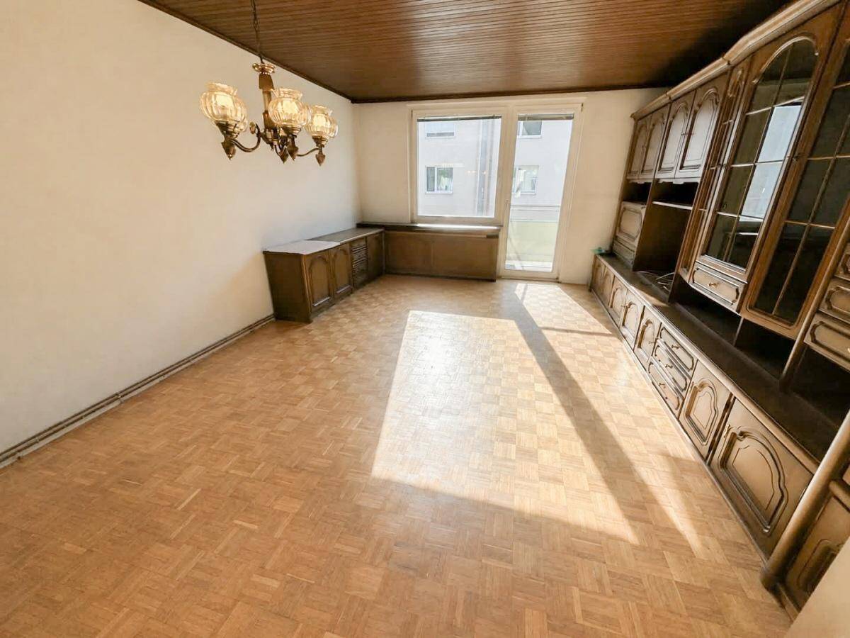 Geräumiges Wohnzimmer mit Fischgrätparkett, Holzdecke und Zugang zu einem kleinen Balkon.
