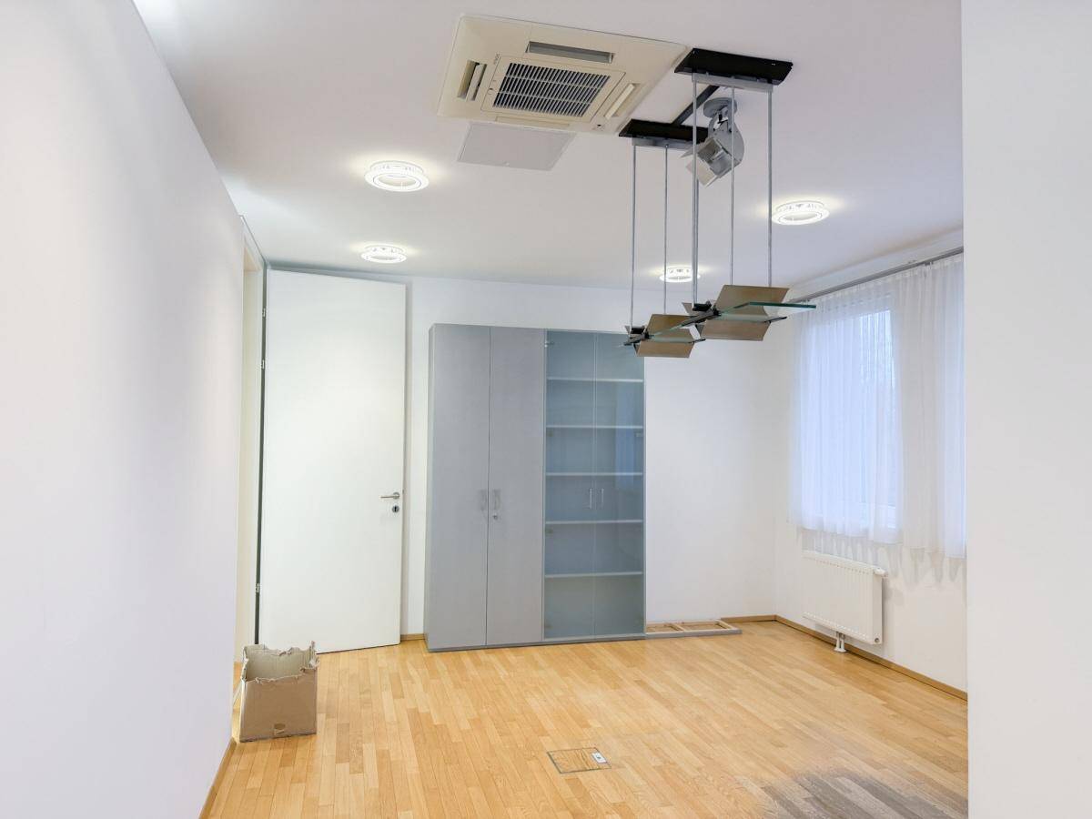 Heller Büroraum mit Holzboden, Einbauschrank und Klimaanlage an der Decke.