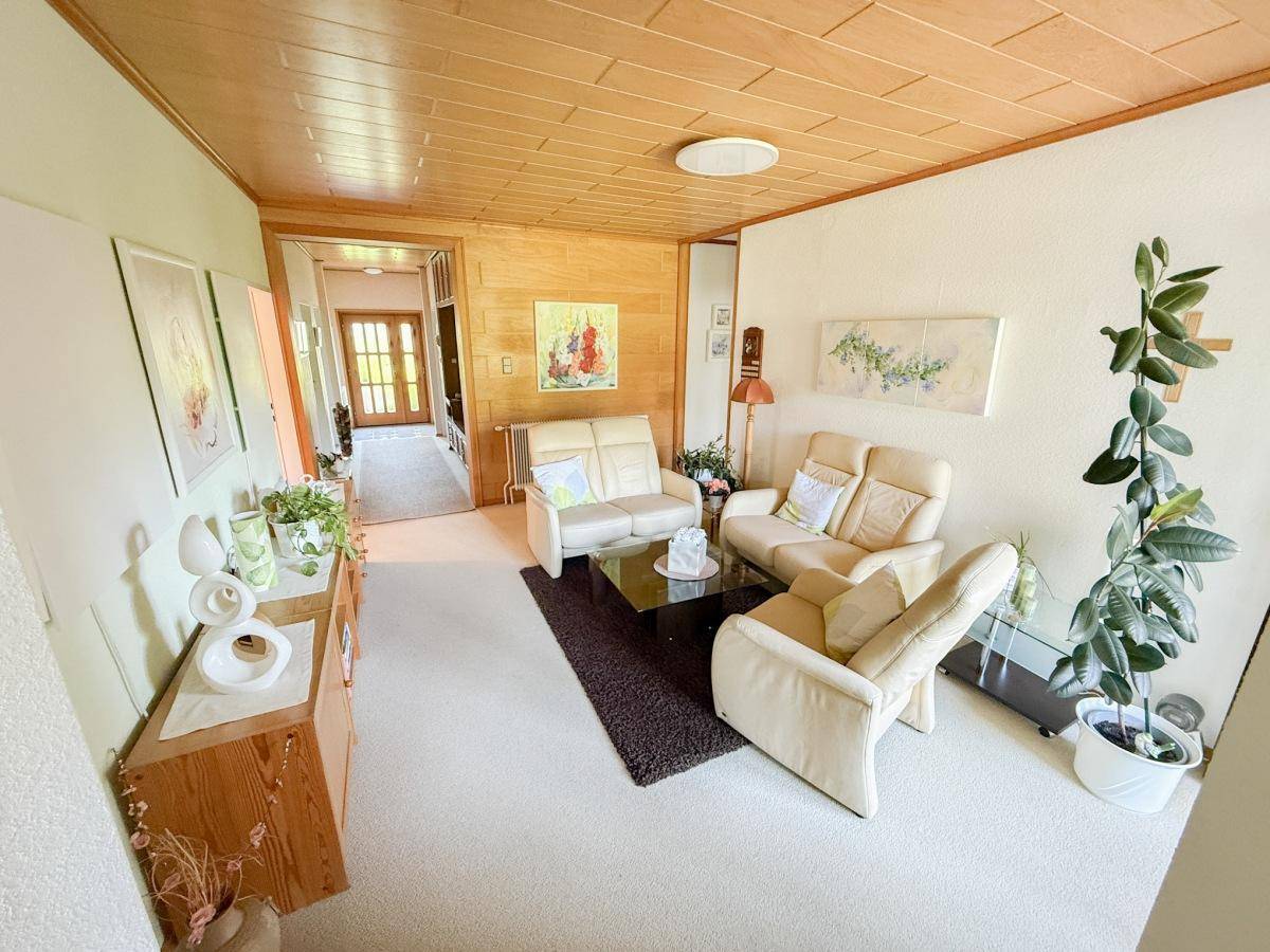 Helles Wohnzimmer mit beigem Teppichboden, Holzdecke und bequemen Sofas.