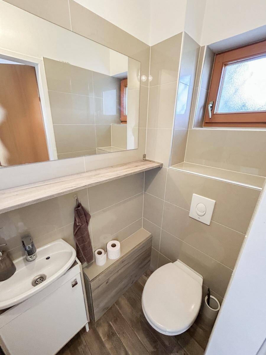 Modernes Gäste-WC mit beigen Fliesen, Waschbecken und Fenster.