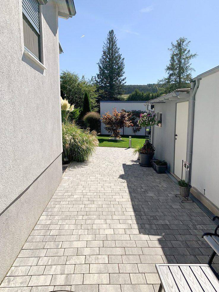 Gepflasterter Weg zwischen zwei Gebäuden, der zum hinteren Gartenbereich führt.