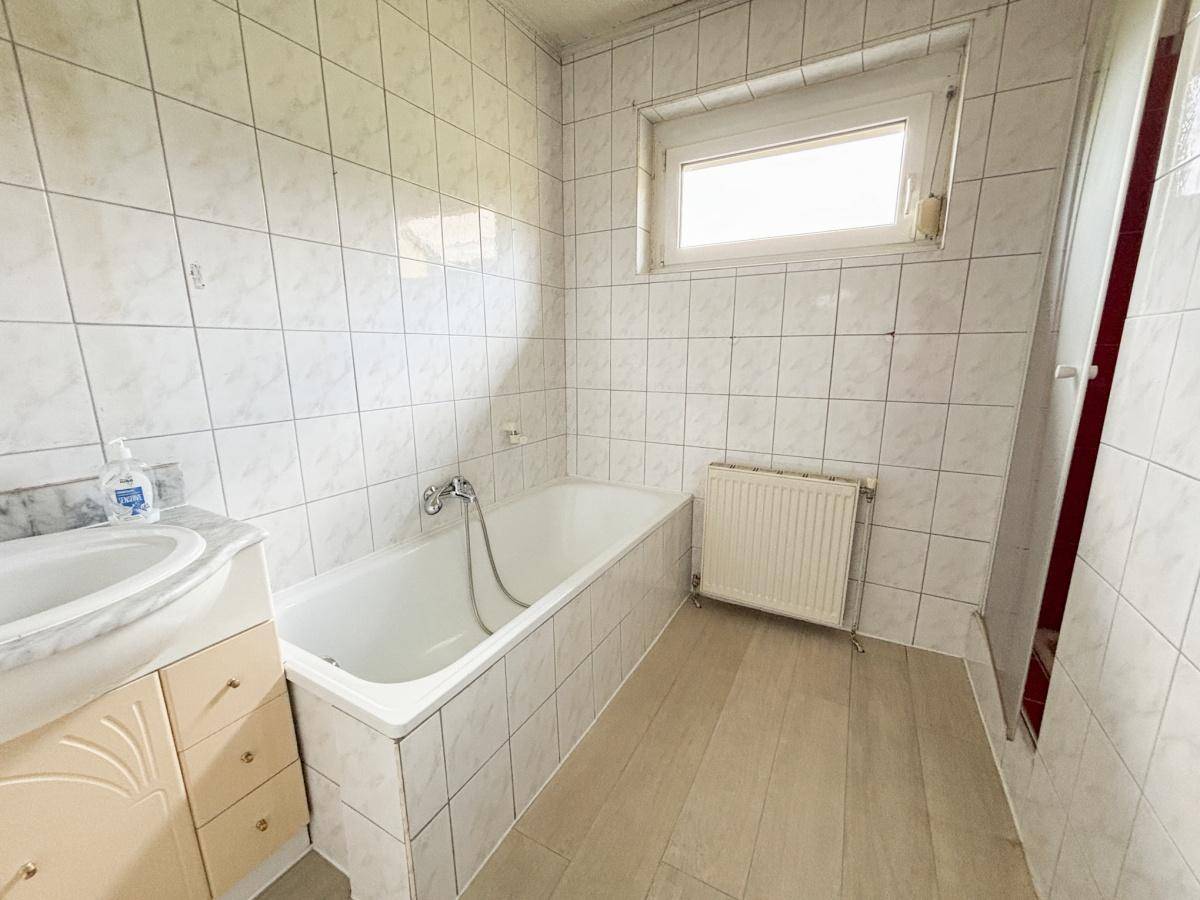 Gefliestes Badezimmer mit Badewanne, Waschbecken und Fenster für natürliche Belüftung.