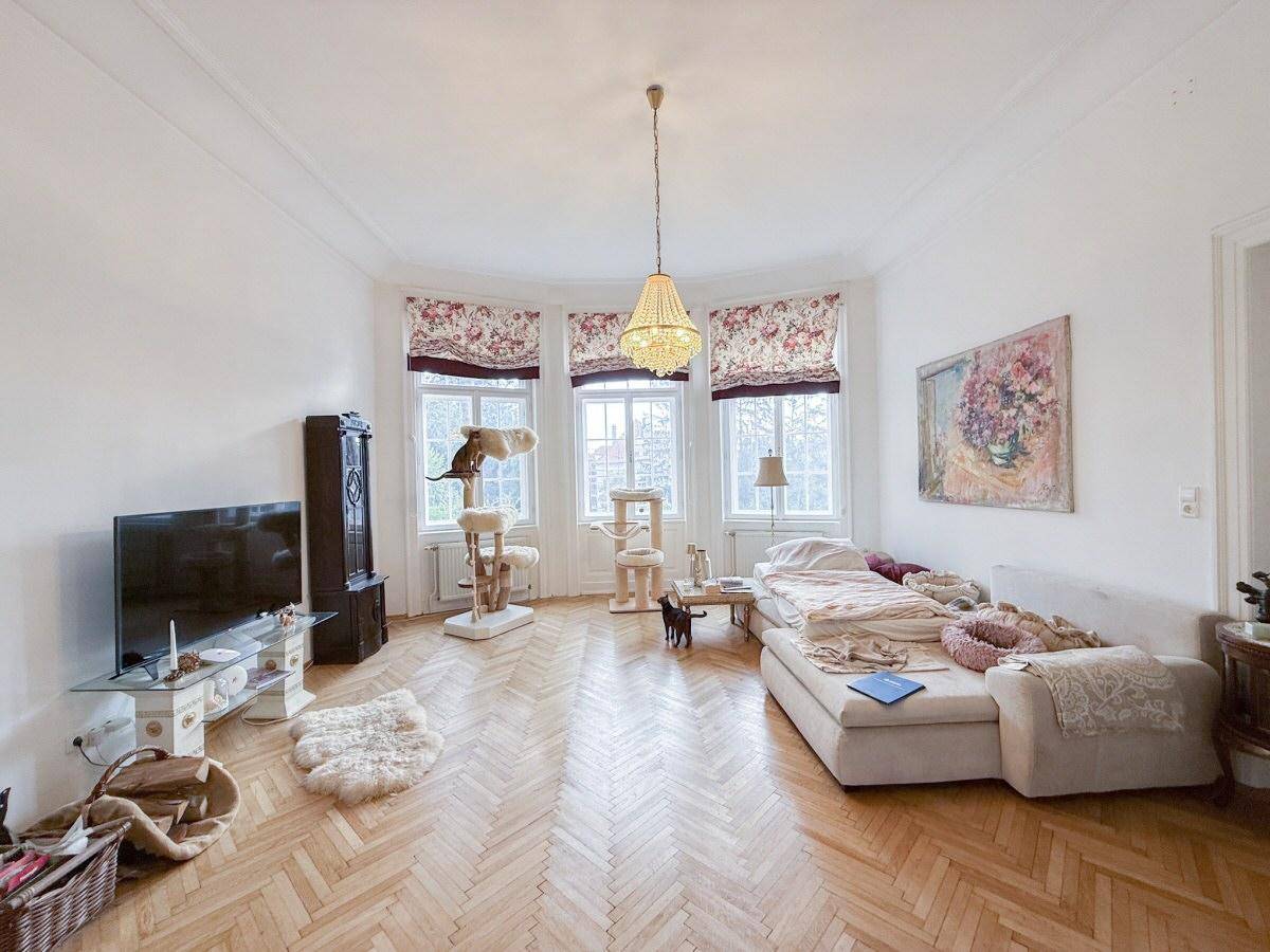 Geräumiges Wohnzimmer mit Fischgrätparkett, Erkerfenstern und gemütlicher Sitzecke.