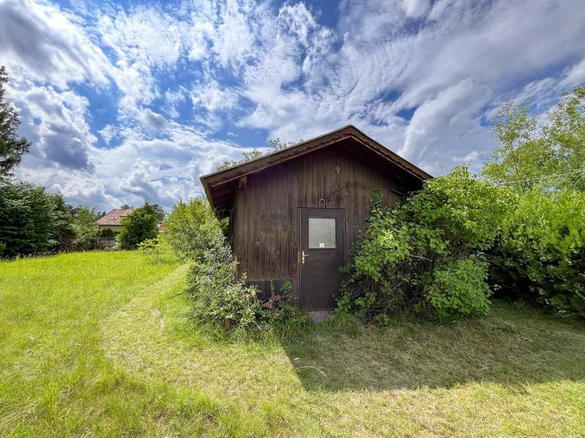 Rustikaler Holzschuppen umgeben von Grünflächen unter einem bewölkten Himmel.