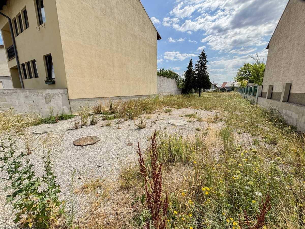 Detailansicht des unbebauten Grundstücks mit Kies, Wildwuchs und sichtbaren Kanaldeckeln.