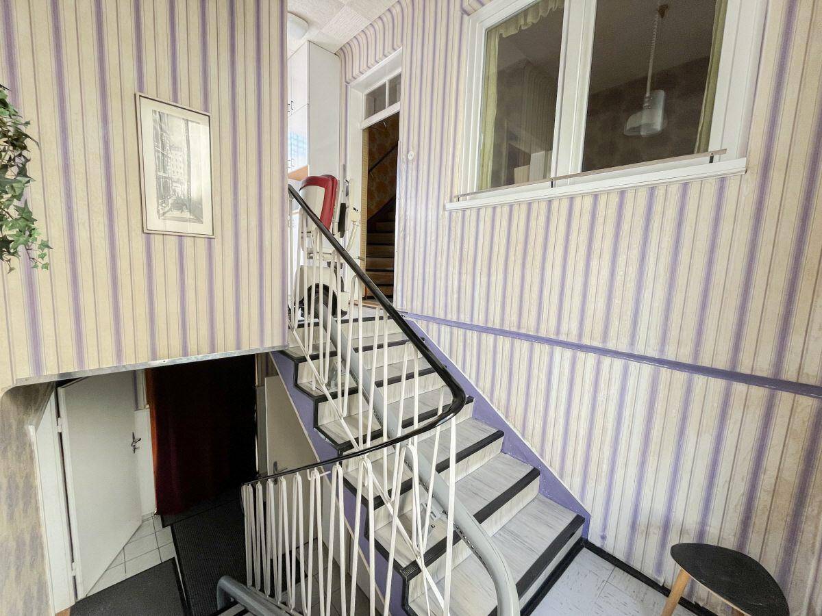 Treppenhaus mit gestreifter Tapete, Holzgeländer und Zugang zu verschiedenen Etagen.