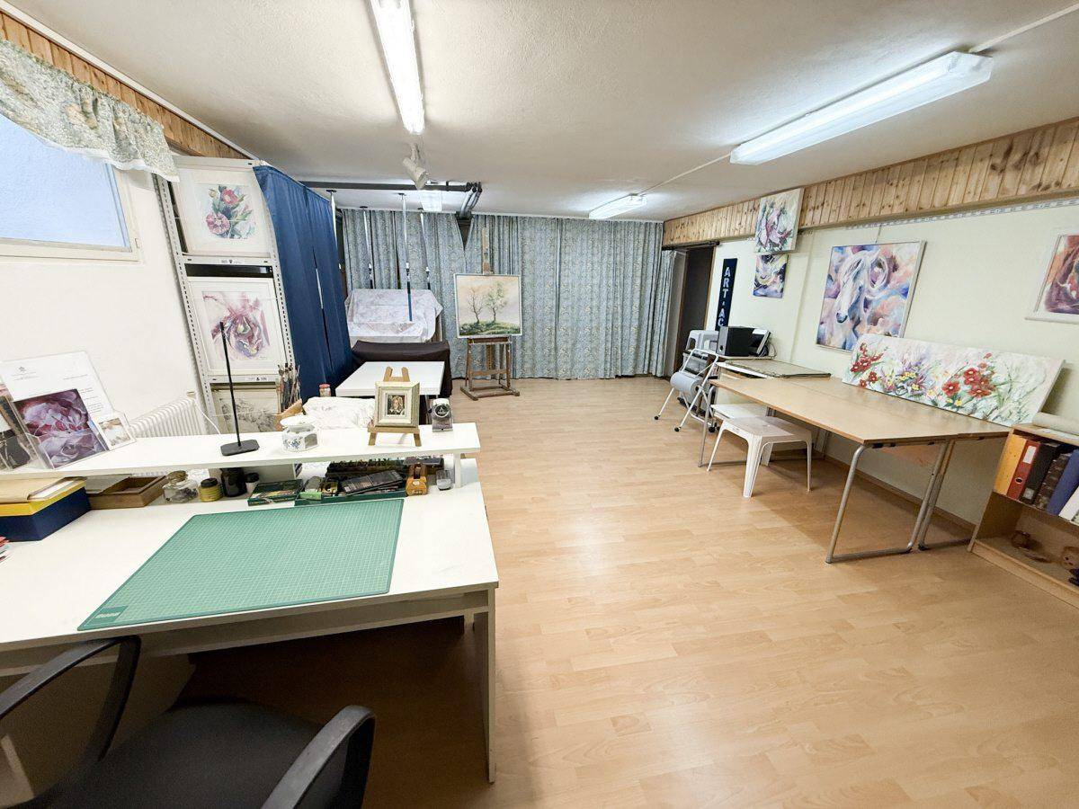 Heller Hobbyraum oder Büro mit Holzboden, Arbeitstischen und Kunstwerken an den Wänden.