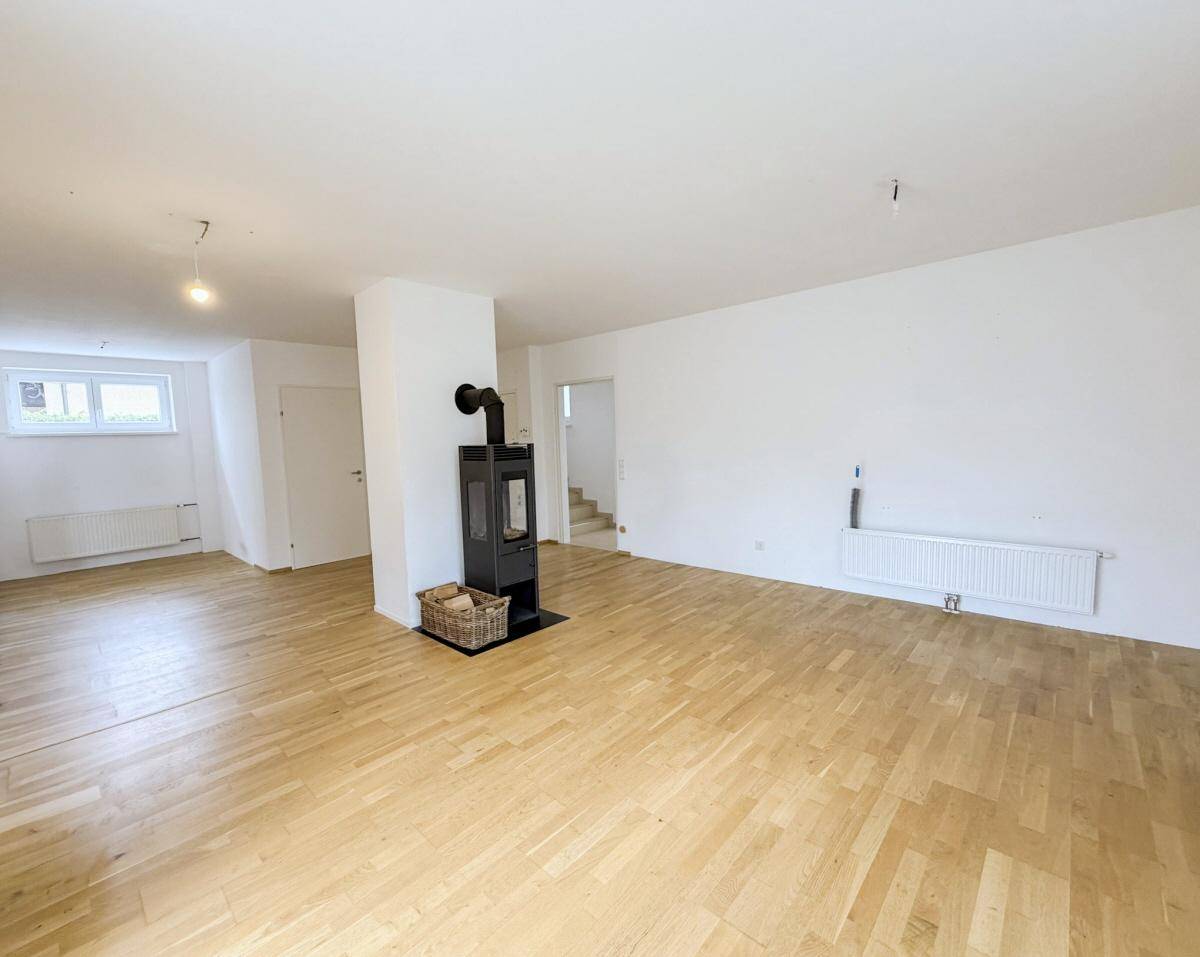 Geräumiges Wohnzimmer mit Holzboden und Kaminofen, bereit zur individuellen Gestaltung.