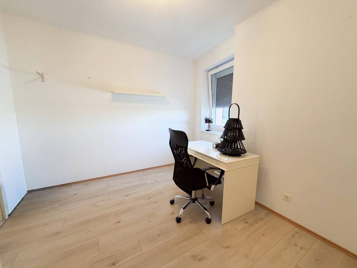 Helles Arbeitszimmer mit Schreibtisch, Bürostuhl und Fenster mit Rollladen.