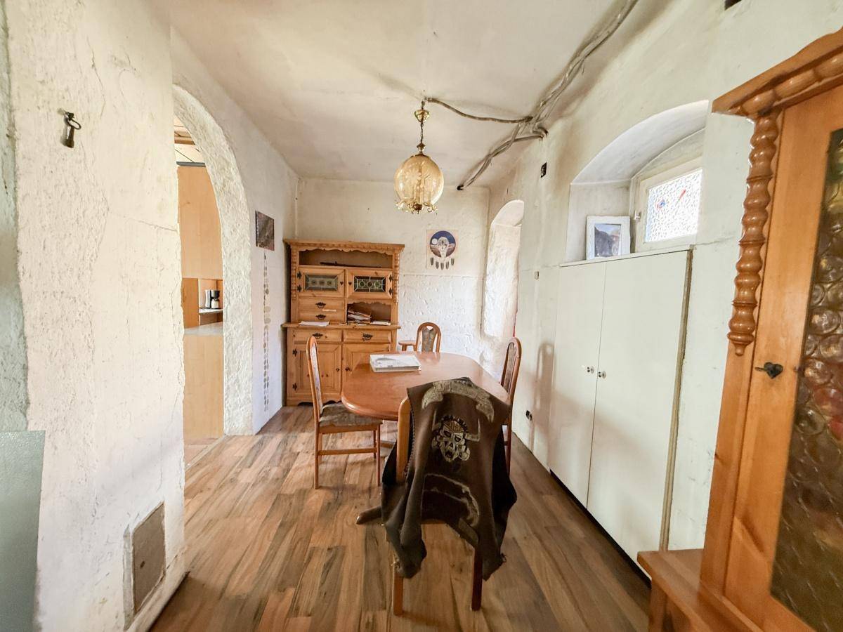 Esszimmer mit Holztisch, Stühlen und traditionellen Holzmöbeln, mit Blick auf den angrenzenden Küchenbereich.