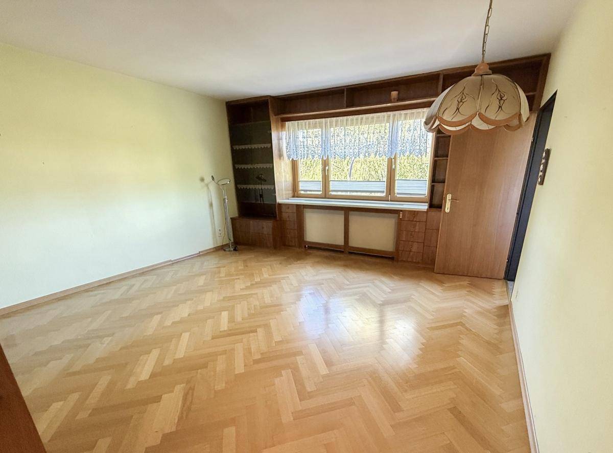Geräumiges Zimmer mit Fischgrätparkett, Einbauregalen und großem Fenster, ideal als Wohn- oder Arbeitszimmer.