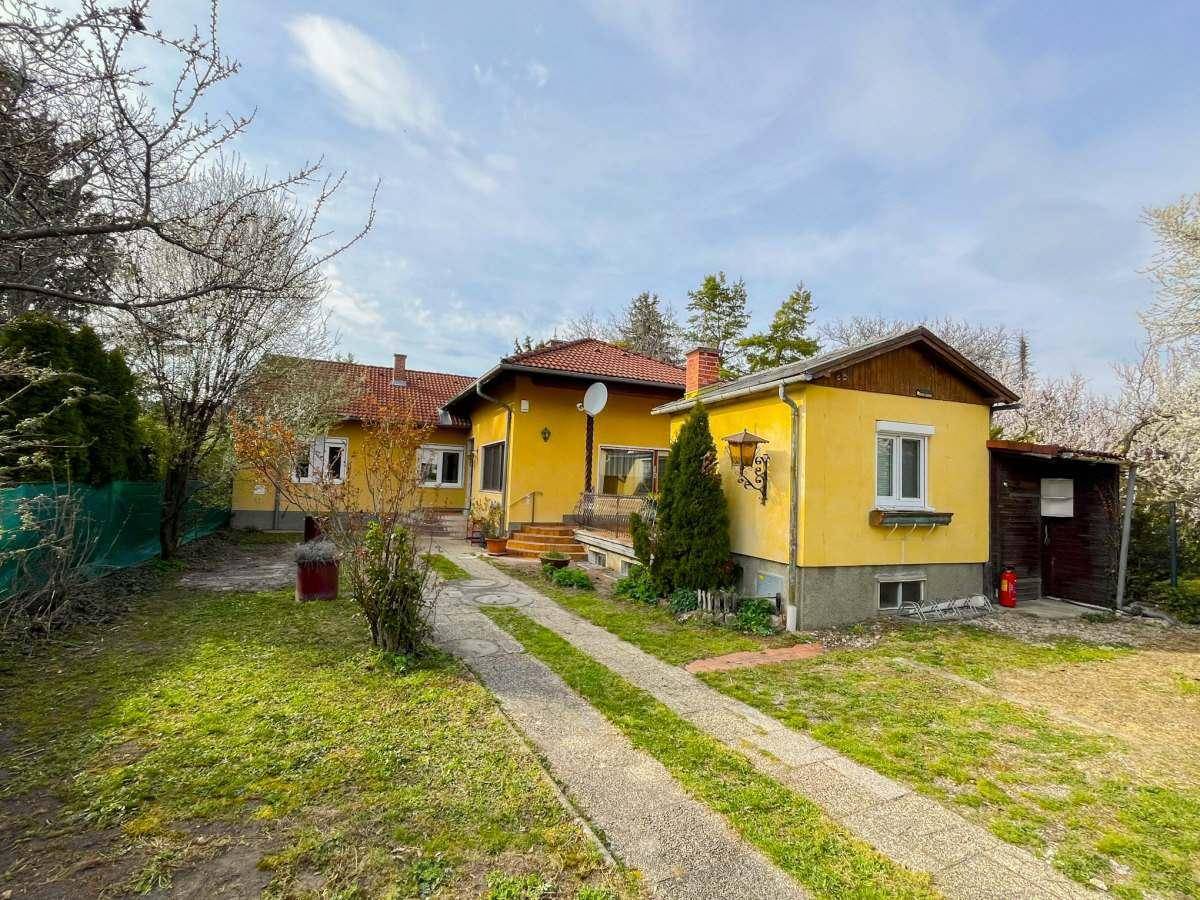 Gelbes Einfamilienhaus mit Garten, Nebengebäude und gepflegter Grünfläche.