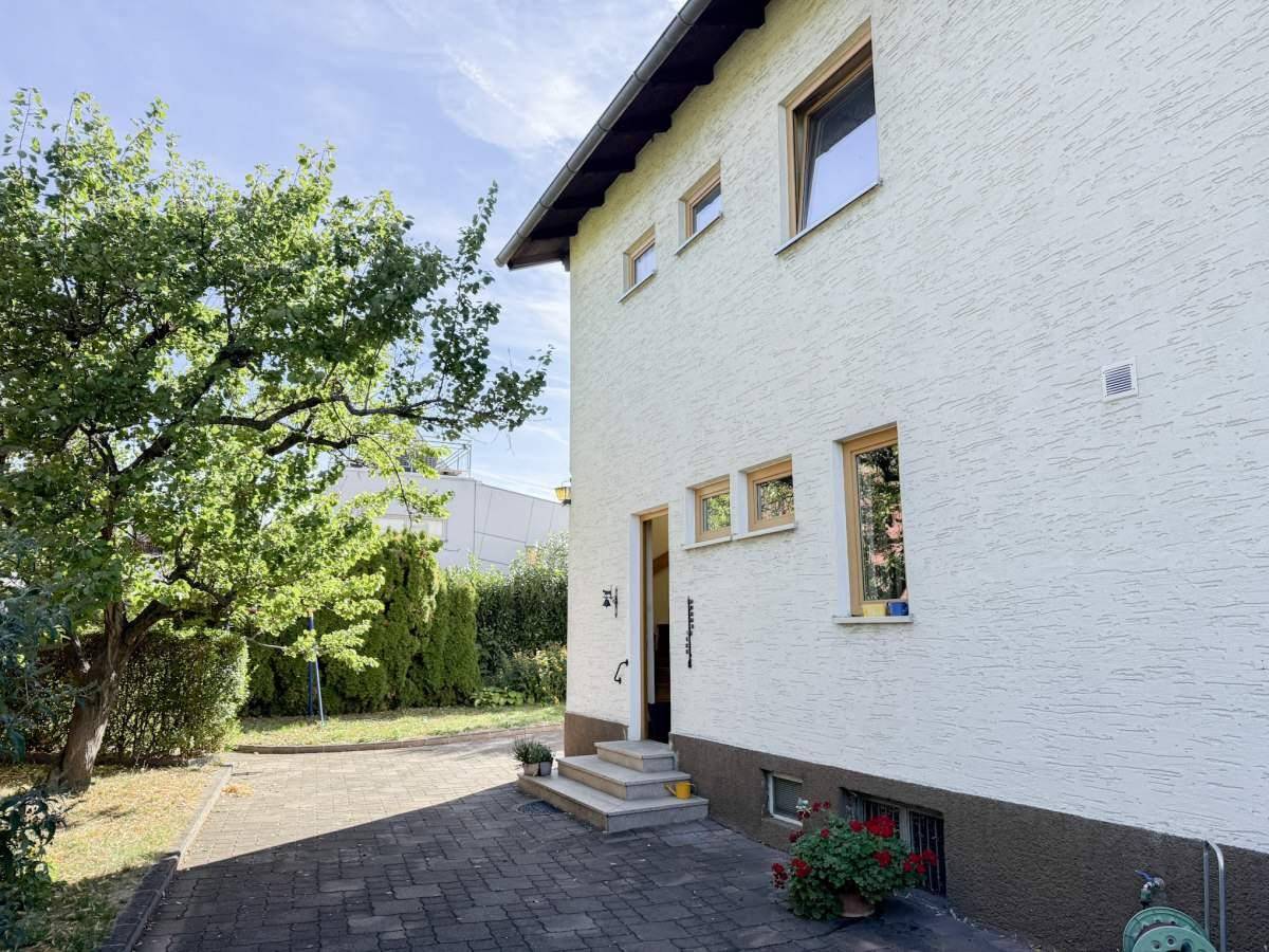 Seitlicher Eingangsbereich des Hauses mit gepflastertem Weg und Zugang zum Garten.
