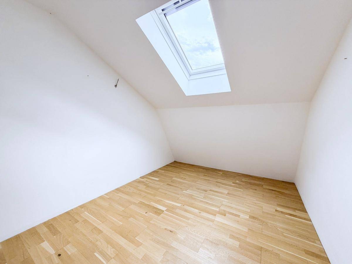 Dachzimmer mit Holzboden und Dachfenster, das viel natürliches Licht hereinlässt.