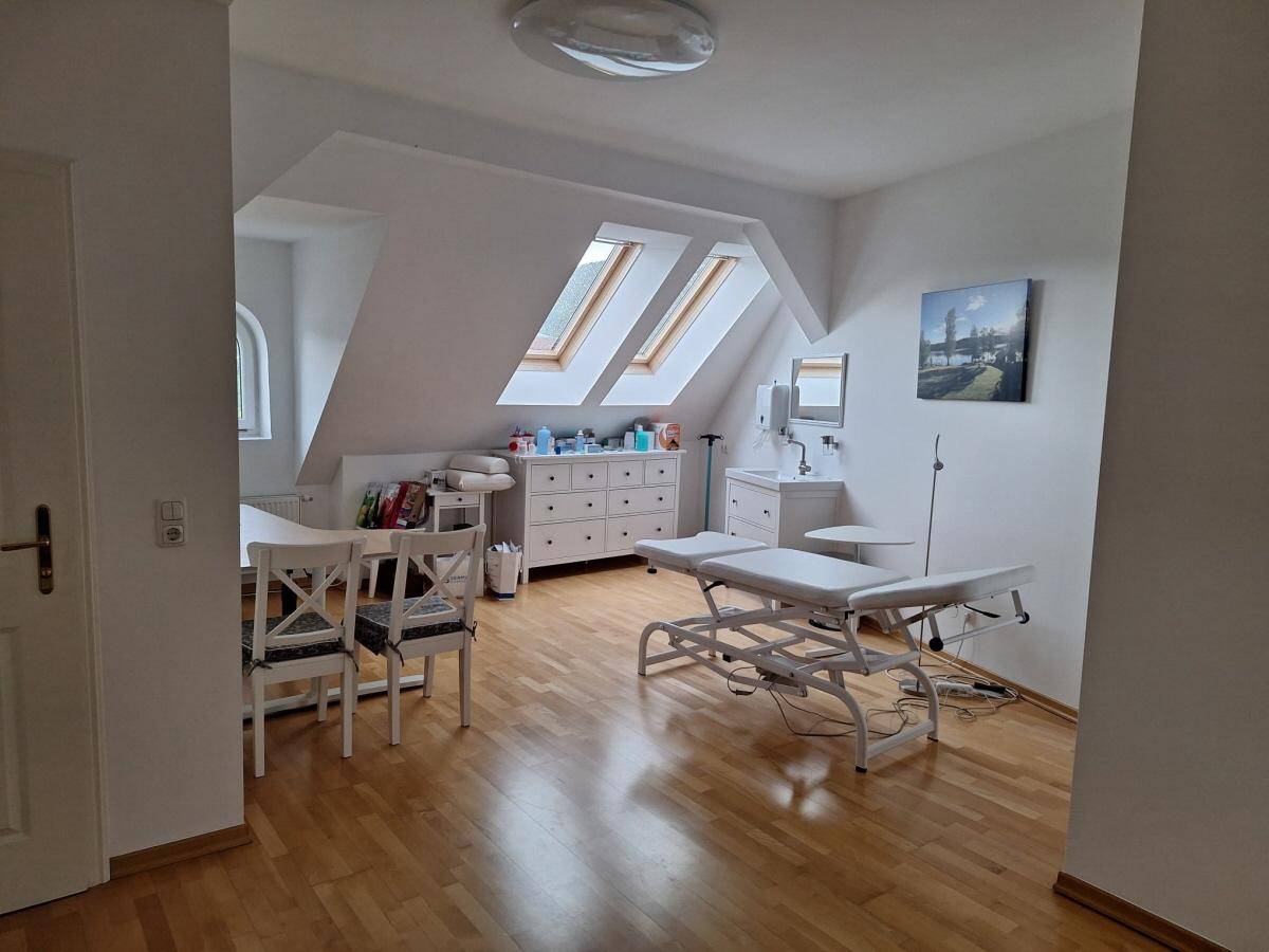 Geräumiges Büro im Dachgeschoss mit Holzboden, Dachfenstern und einer Untersuchungsliege, ideal für Praxisräume.