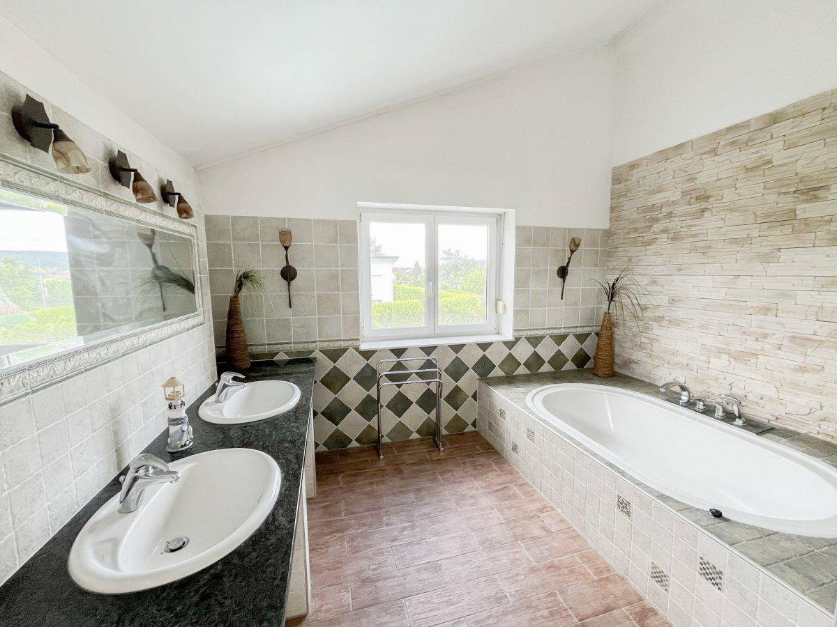 Geräumiges Badezimmer mit Doppelwaschbecken, eingebauter Badewanne und Fenster mit Ausblick.