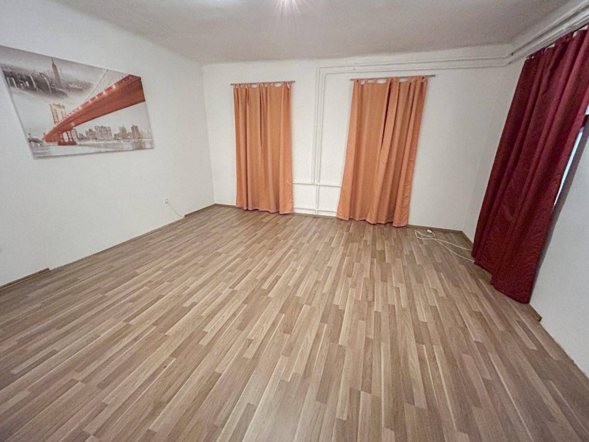 Leerer Raum mit Laminatboden, weißen Wänden und orangefarbenen Vorhängen an den Fenstern.