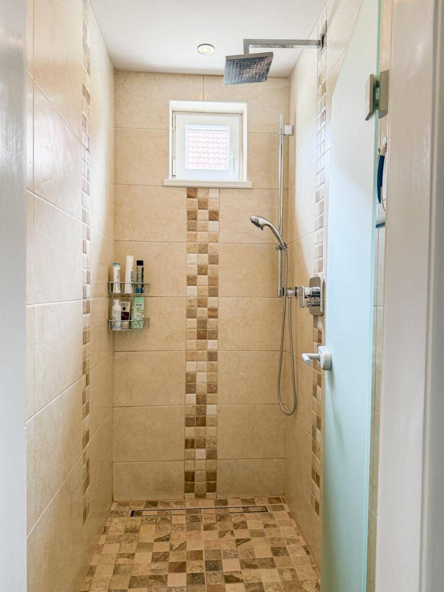 Moderne Duschkabine mit beigefarbenen Fliesen, Regendusche und kleinem Fenster für natürliches Licht.