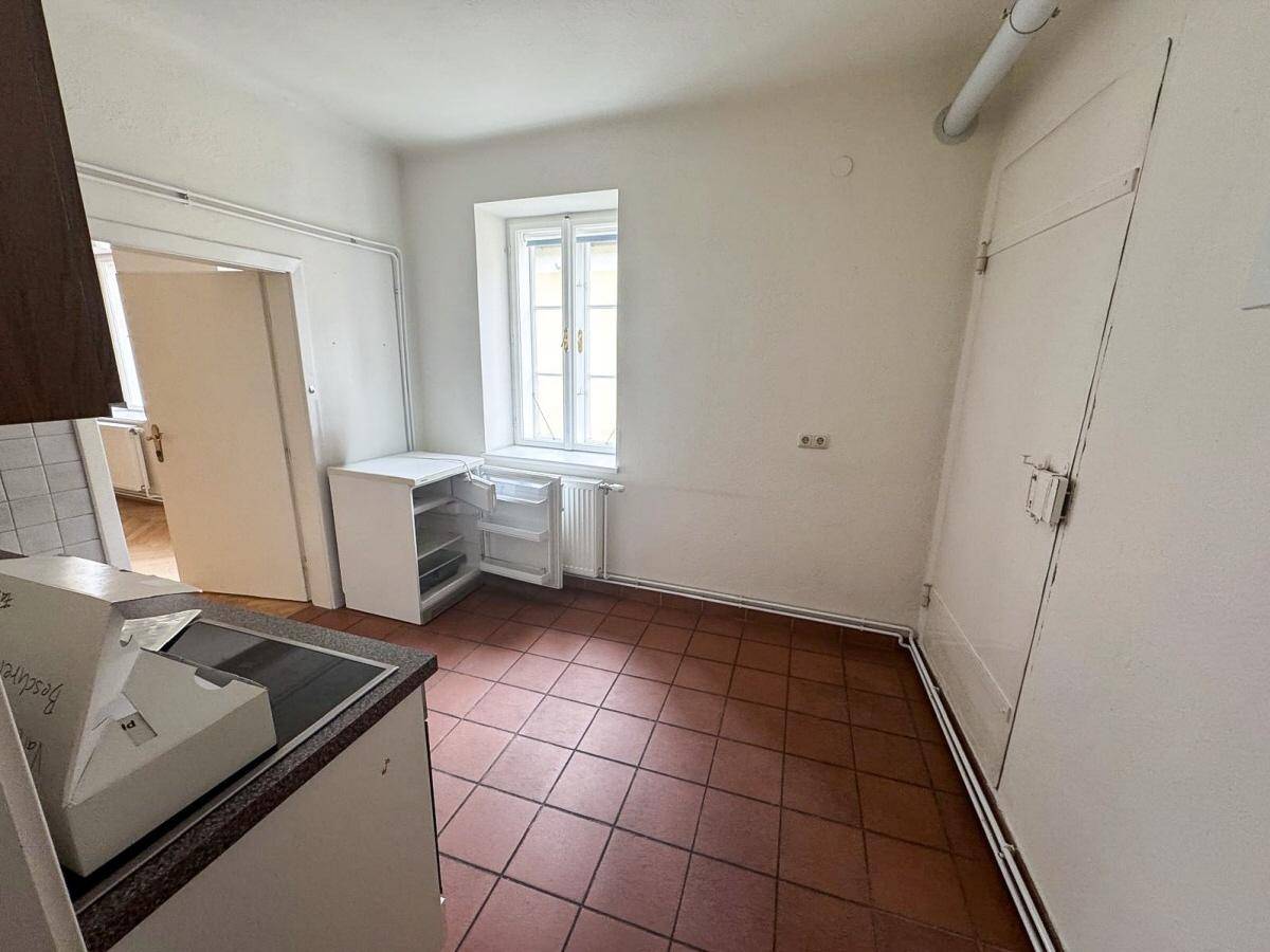 Einfache Küche mit Terrakotta-Fliesenboden, einem Fenster und einem kleinen Kühlschrank.