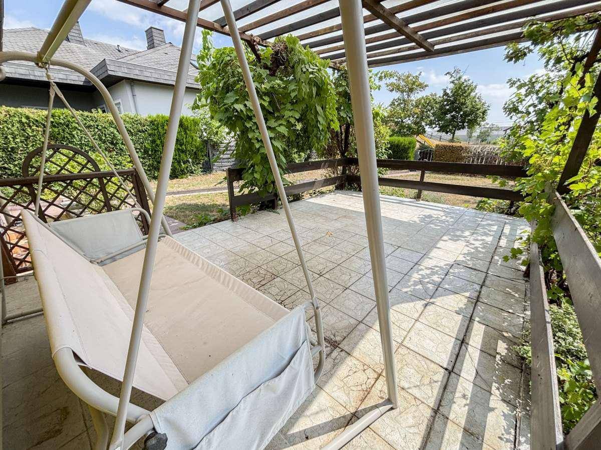 Überdachte Terrasse mit Schaukelbank und Blick in den Garten, ideal zum Entspannen.