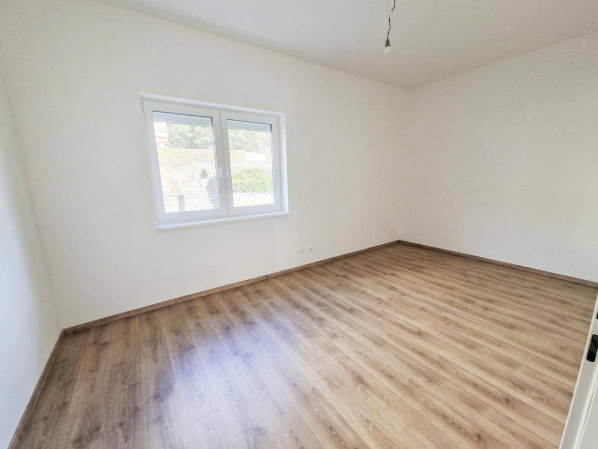 Unmöbliertes Schlafzimmer mit Laminatboden und einem großen Fenster, das viel Licht hereinlässt.