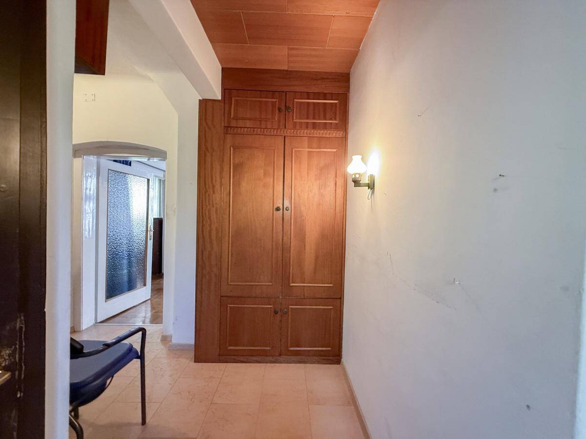 Flur mit Einbauschrank aus Holz und hellen Fliesenboden, führt zu weiteren Räumen.