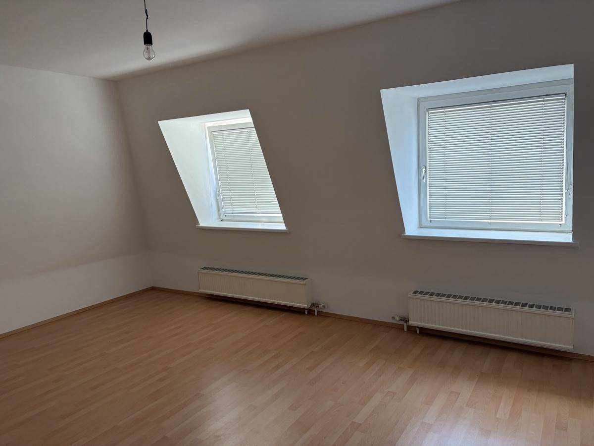 Heller Raum mit zwei Dachfenstern, Dachschrägen und Laminatboden, bereit zur Einrichtung.