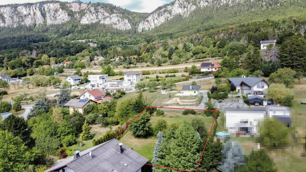 Luftaufnahme eines Baugrundstücks mit Bergblick, umgeben von Wohnbebauung und grüner Natur.