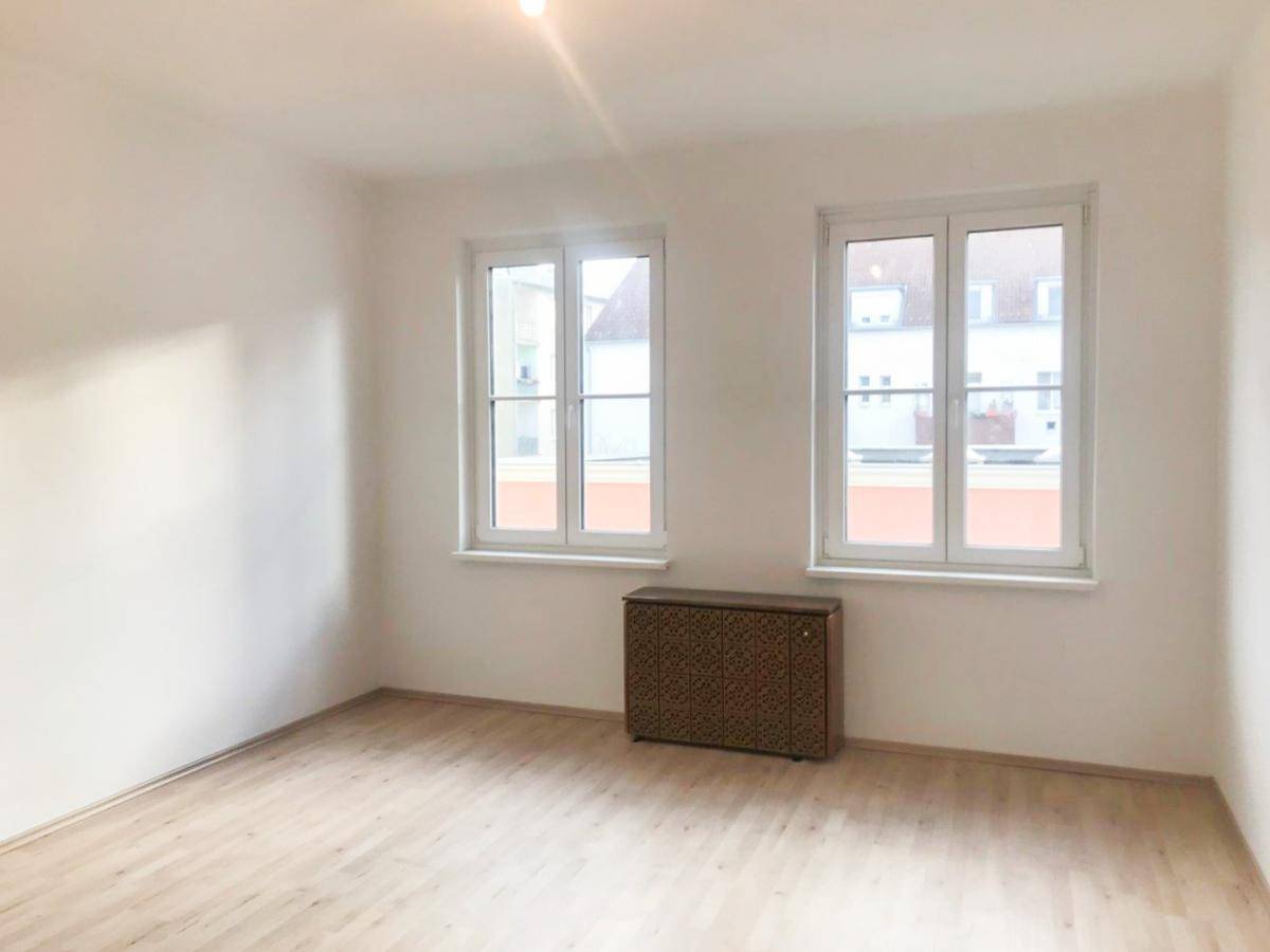 Ein heller, leerer Raum mit zwei großen Fenstern und Laminatboden, bereit zur individuellen Gestaltung.