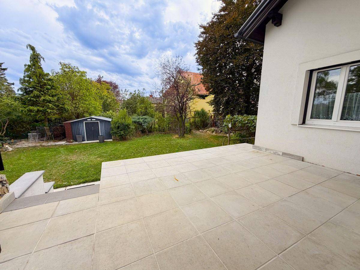 Große geflieste Terrasse mit Blick auf den Garten und den Geräteschuppen.