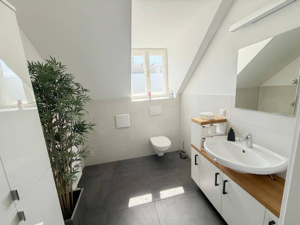 Modernes Badezimmer im Dachgeschoss mit Dachschräge, Fenster, WC und Waschtisch mit Holzplatte.