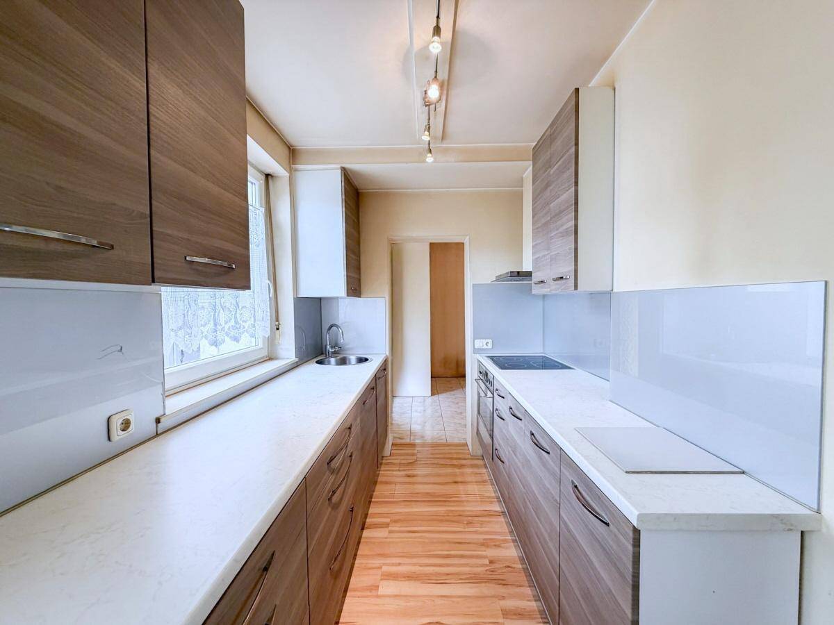 Schmale Küche mit Holzschränken, hellen Arbeitsplatten und Laminatboden.