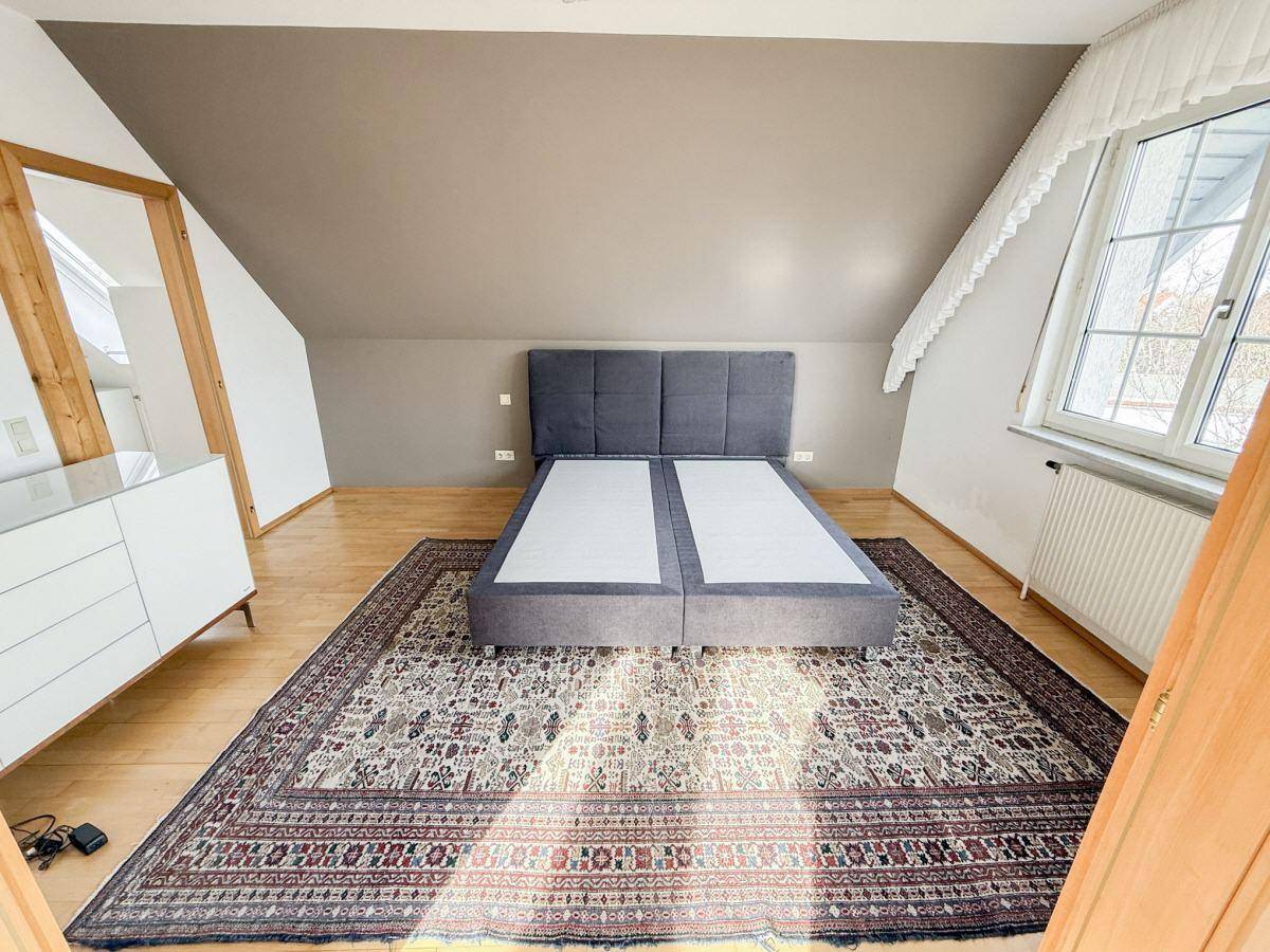 Gemütliches Schlafzimmer im Dachgeschoss mit Holzdielenboden, Dachschräge und großem Teppich.