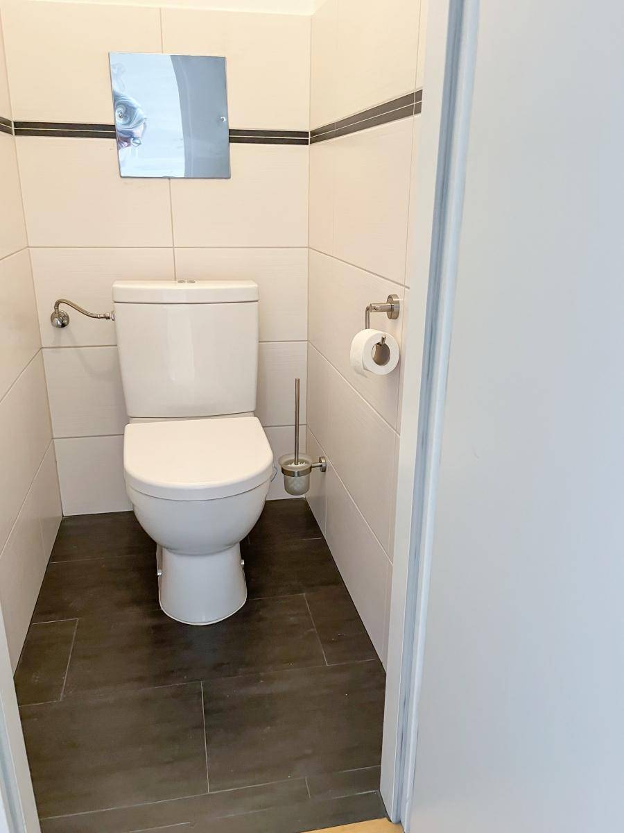 Separates WC mit wandmontierter Toilette und dunklen Bodenfliesen.